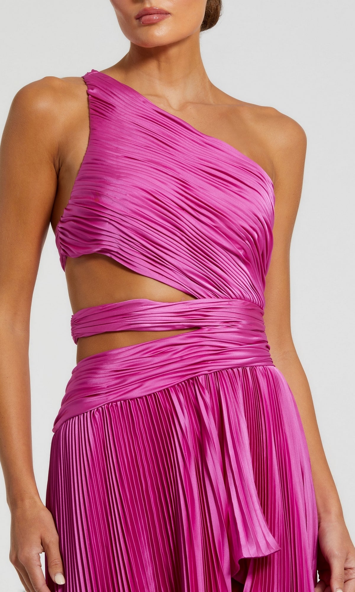 A person wearing the Mac Duggal 49837 High-Low Pleated Formal Dress, featuring a vibrant pink hue, one-shoulder cut-out design, pleats, waist cutout, and wrapped draped details.
